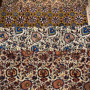 May include: A folded textile with intricate floral and geometric patterns in shades of red, blue, yellow, and white. The design includes repeating floral motifs and star-like shapes. The textile has a fringed edge.