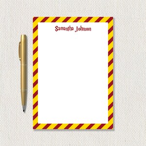 May include: A personalized notepad with a white interior and a border of alternating yellow and maroon diagonal stripes. The name "Samantha Johnson" is printed in maroon script at the top. A gold pen rests on the left side.