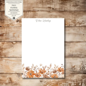 May include: A personalized fall floral notepad with a watercolor design. The notepad features a border of orange and brown flowers and foliage. The notepad is 5" x 7" and contains 50 sheets. The name "Clare Lindsey" is printed at the top.