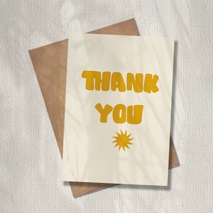 May include: A cream-colored greeting card with the words "THANK YOU" in bold, yellow letters. A yellow starburst design is below the text. The card is paired with a brown envelope.