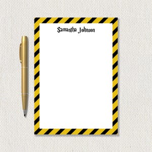 May include: A gold pen rests beside a white notepad with a yellow and black striped border. The notepad has the name "Samantha Johnson" printed in black script at the top.