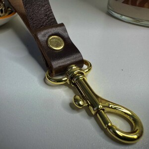 May include: A brown leather strap with a gold metal clasp. The strap has a gold metal button on the front.