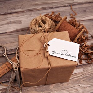 May include: A brown paper-wrapped gift box tied with twine and a white gift tag that reads "Love, Santa Claus". The box is surrounded by brown packing paper and twine.