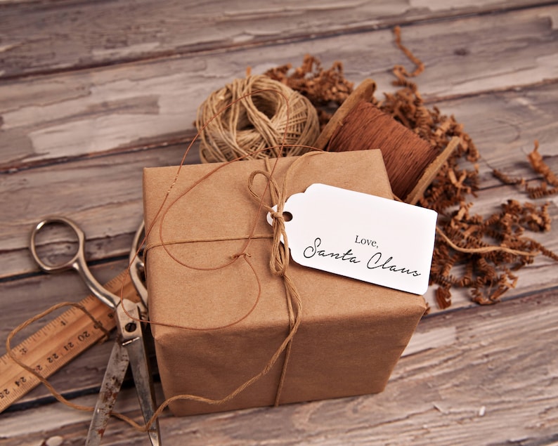 May include: A brown paper-wrapped gift box tied with twine and a white gift tag that reads "Love, Santa Claus". The box is surrounded by brown packing paper and twine.