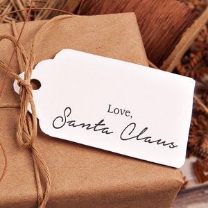 May include: A brown paper gift bag with a white tag tied with twine. The tag has the text "Love, Santa Claus" written in black cursive.