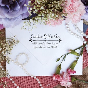 May include: White envelope with a black ink return address stamp that reads "Eddie & Katie 420 Lovely Tree Lane Glendora, CA 91842". The envelope is surrounded by pink and white flowers and a pearl necklace.