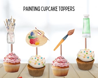 Può includere: Cupcake con glassa rosa e bianca, decorati con zuccherini colorati. Ogni cupcake ha un topper a tema pittura: pennelli, una tavolozza, un pennello e un tubetto di vernice. Testo: "PAINTING CUPCAKE TOPPERS".
