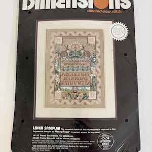 Puede incluir: Un kit de punto de cruz contado Dimensions titulado Linen Sampler, que presenta un diseño con dos conejos marrones, motivos florales y letras del alfabeto sobre tela de lino. El empaque incluye texto, un gráfico con acento de color y medidas.