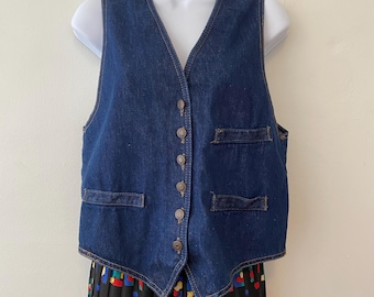 May include: A dark blue denim vest with a V-neck and four pockets. The vest has five brown buttons down the front and is displayed on a white mannequin. The vest is a classic style.