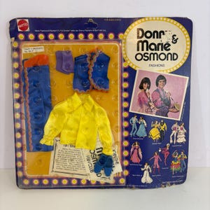 May include: Vintage Mattel Donny & Marie Osmond doll fashion set. The set includes a yellow shirt, blue pants, a blue vest, purple accessories, and blue shoes. The packaging features a photo of the duo and the text "South the Border".