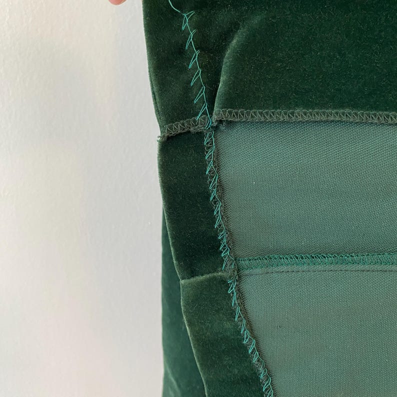 Puede incluir: Primer plano de una tela de terciopelo verde oscuro con un forro verde oscuro contrastante. La tela est&aacute; cosida con una puntada visible.
