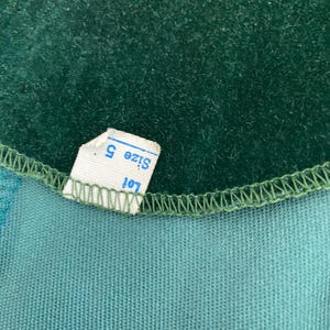 Puede incluir: Primer plano de una tela de terciopelo verde con una etiqueta blanca que dice "Talla S" y "Lote 101".