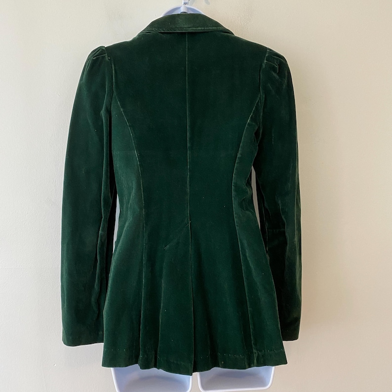 Puede incluir: Una chaqueta de terciopelo verde oscuro con un corte cl&aacute;sico. La chaqueta tiene un cuello de muesca, mangas largas y un cierre de un solo bot&oacute;n.