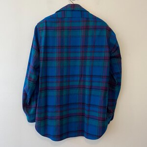 Pu&ograve; includere: Una camicia a quadri blu, verde e viola. La camicia a maniche lunghe ha un colletto. Il motivo a quadri &egrave; un design classico, con linee che si intersecano creando un motivo a griglia. La camicia &egrave; realizzata in un materiale morbido, forse flanella.