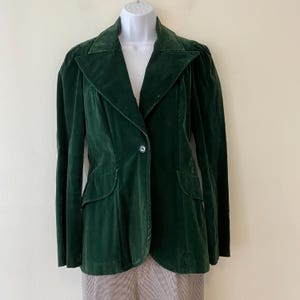 Puede incluir: Una chaqueta de terciopelo verde oscuro con un cierre de bot&oacute;n &uacute;nico y un cuello puntiagudo. La chaqueta tiene una silueta ajustada y presenta dos bolsillos en la parte delantera.