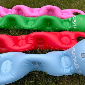 Może przedstawiać: Cztery nadmuchiwane materace do pływania w różnych kolorach: różowym, zielonym, czerwonym i niebieskim. Każdy materac ma falisty wzór i napis "FLOODLES" nadrukowany na nim.