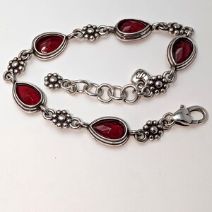 May include: Silver-toned bracelet featuring teardrop-shaped, deep red gemstones. The bracelet has a floral design between each gemstone and a secure clasp. A beautiful piece of jewelry.