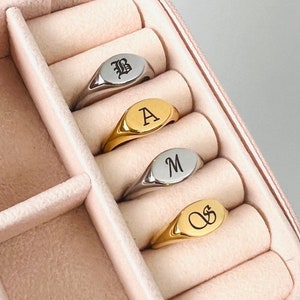 May include: Four signet rings in a pink velvet ring box. The rings are made of silver and gold and feature the letters B, A, M, and a cursive S.