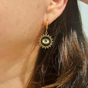 Op de afbeelding: Gouden creolen met een zwart-witte kwade oog-bedel in de vorm van een zon.
