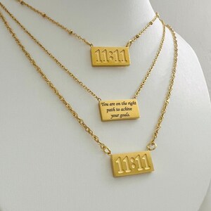 May include: Gold layered necklace with three rectangular pendants. The top pendant says "11:11". The middle pendant says "You are on the right path to achieve your goals". The bottom pendant says "11:11".
