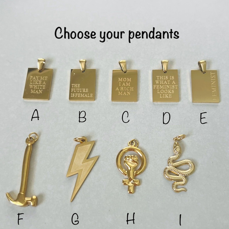 May include: Nine gold pendants with different designs and text. The pendants are arranged in two rows of five. The top row includes pendants with the text "Pay me like a white man", "The future is female", "Mom I am a rich man", "This is what a feminist looks like", and "Feminist". The bottom row includes pendants with a hammer, lightning bolt, female symbol with a fist, snake, and a blank pendant.