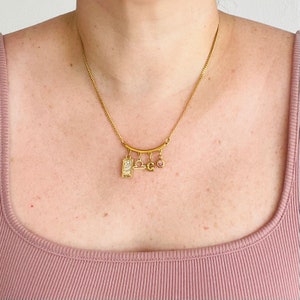 Peut inclure: Collier en or avec un pendentif zodiaque Balance, un petit pendentif lettre 'G' et un pendentif en cristal rose.