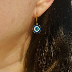 Op de afbeelding: Gouden creolen met een blauwe en witte kwade oog bedel. De bedel heeft een witte kern met een blauw oog en een blauwe buitenring.