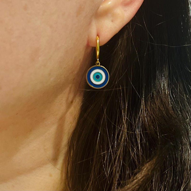 Op de afbeelding: Gouden creolen met een blauwe en witte kwade oog bedel. De bedel heeft een witte kern met een blauw oog en een blauwe buitenring.