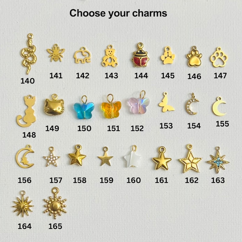 May include: A selection of gold-tone charms with various designs, including a snake, bee, elephant, bear, ladybug, paw print, cat, butterfly, crescent moon, star, and sun. Each charm is numbered from 140 to 165.