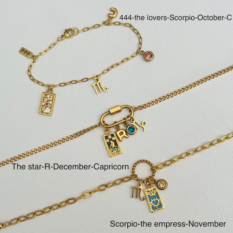 May include: Three gold chain bracelets with charms. The top bracelet has a pink gemstone and the text "444-the lovers-Scorpio-October-C". The middle bracelet has a blue gemstone and the text "The star-R-December-Capricorn". The bottom bracelet has a gold charm with the text "Scorpio-the empress-November".