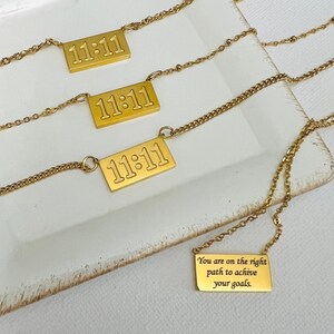 May include: Three gold necklaces with rectangular pendants. The pendants have the number 11:11 engraved on them. The fourth necklace has a pendant with the text "You are on the right path to achieve your goals".