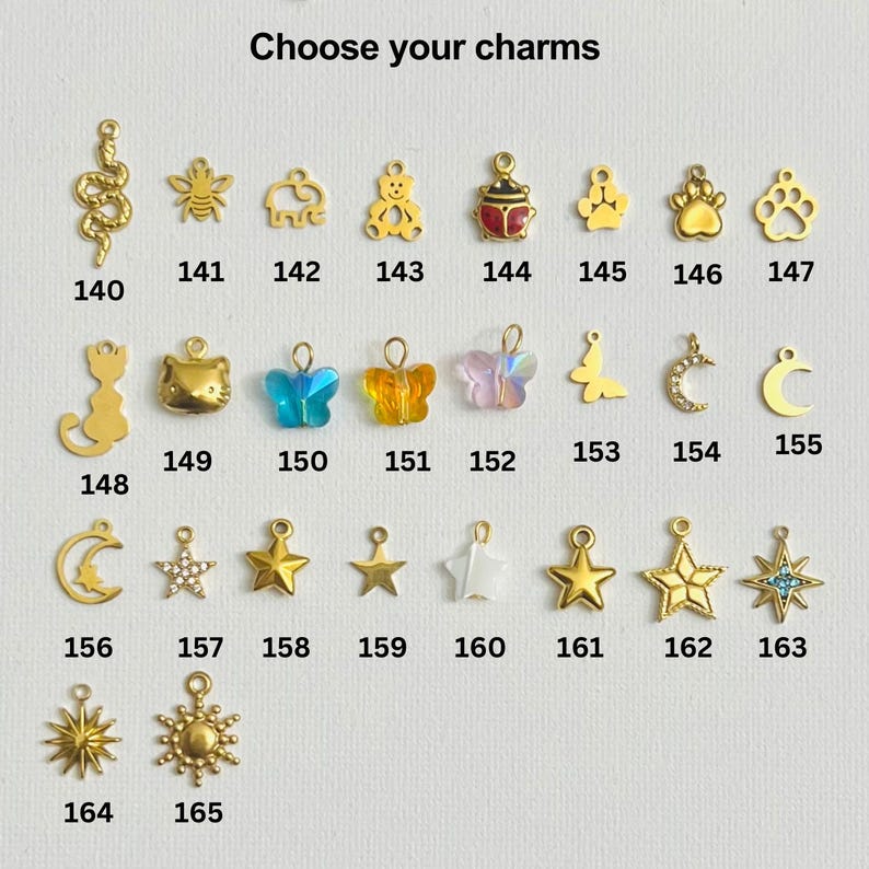 May include: A selection of gold-toned charms with various designs, including a snake, bee, elephant, bear, ladybug, paw print, cat, butterfly, crescent moon, star, and sun. Each charm is numbered from 140 to 165.