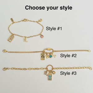 May include: Three gold chain bracelets with different charms. The first bracelet has a pink stone, a letter "C" charm, and a tarot card charm. The second bracelet has a carabiner clasp, a tarot card charm, and a charm that says "ROMY". The third bracelet has a round charm, a tarot card charm, and a letter "M" charm. The bracelets are labeled "Style #1", "Style #2", and "Style #3".