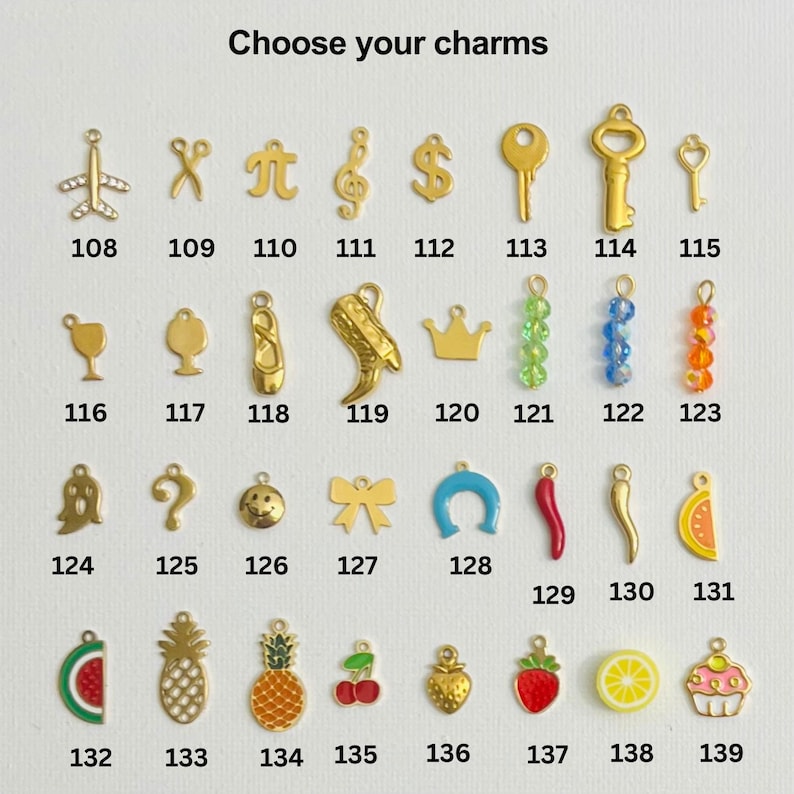 May include: A chart of gold charms with numbers 108 to 139. The charms include a variety of shapes, such as airplanes, keys, musical notes, crowns, and fruit. Choose your charms.