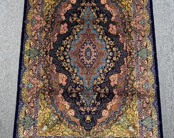 May include: An intricately patterned rug with a central medallion design. The rug has a navy blue border and a complex pattern in gold, teal, pink, and brown. White fringe trims the short ends, adding a decorative element.