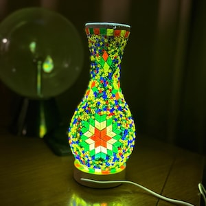 May include: A colorful mosaic glass lamp with a star design. The lamp is lit and casting a warm glow on the table.