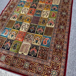 May include: An intricately patterned rug with a repeating design of squares filled with floral and geometric patterns. The colour palette includes red, blue, green, and gold. The rug has a deep red border with floral motifs and white fringe.