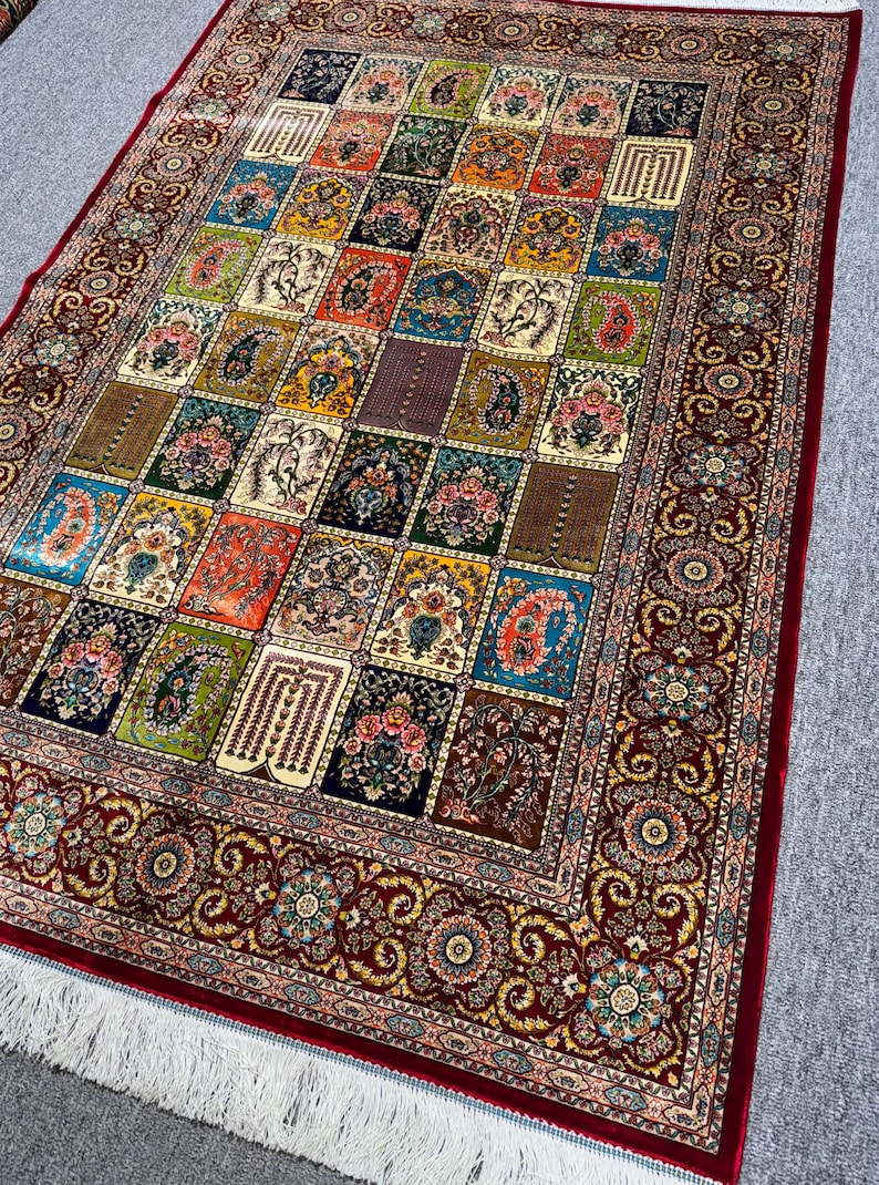 May include: An intricately patterned rug with a repeating design of squares filled with floral and geometric patterns. The colour palette includes red, blue, green, and gold. The rug has a deep red border with floral motifs and white fringe.