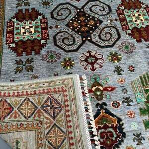 May include: A gray rug with a traditional Persian design featuring intricate patterns in shades of red, blue, green, and brown. The rug has a fringed border and a detailed pattern in the center.