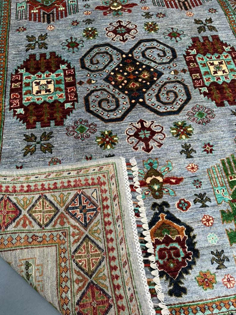 May include: A gray rug with a traditional Persian design featuring intricate patterns in shades of red, blue, green, and brown. The rug has a fringed border and a detailed pattern in the center.