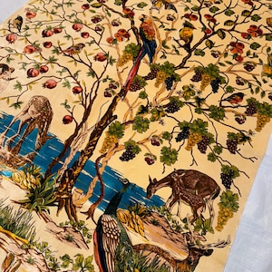 Op de afbeelding: Een cr&egrave;mekleurig tapijt met een gedetailleerd ontwerp van een boom met vogels, druiven en herten. De boom wordt omringd door een blauwe rivier en een pauw. Het tapijt heeft een vintage esthetiek.
