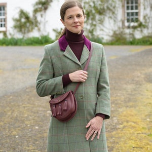 Pu&ograve; includere: Un cappotto in tweed a quadri verde e marrone con un colletto in velluto bordeaux e una borsa in pelle marrone con nappe. Il cappotto ha una chiusura con bottoni ed &egrave; indossato sopra un maglione a collo alto bordeaux.