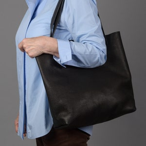 May include: A person carrying a black leather tote bag with a light blue button-down shirt and brown pants.
