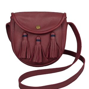 Pu&ograve; includere: Una borsa a tracolla in pelle bordeaux con chiusura a lembo e tre nappine. La borsa ha un bottone dorato e un bordo blu.