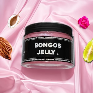 May include: A pink jar with a black lid and label that reads "BONGOS JELLY." The label also says "DO NOT CONSUME ACTIVATOR OR THE SLIME." The jar is on a pink satin background with a coconut half, an almond, a lime slice, and a pink rose.