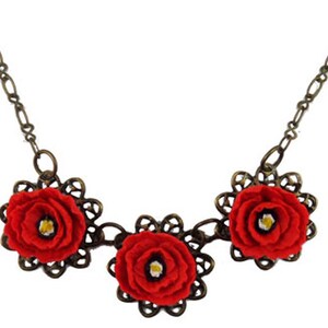 May include: A necklace with three red felt flowers on a bronze chain.