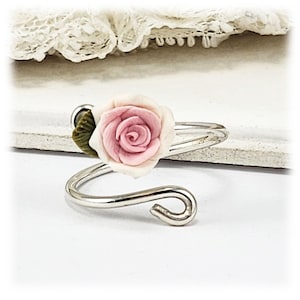 May include: A silver adjustable ring with a pink rose and green leaf charm.