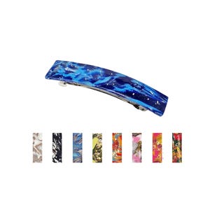 May include: A curved hair barrette featuring a glossy blue marbled pattern with silver flecks. Below, eight additional barrettes are displayed in a row, showcasing various color combinations including black, white, pink, green, and multi-colored patterns.
