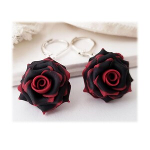 May include: A pair of earrings featuring black and red rose-shaped charms with silver hooks.