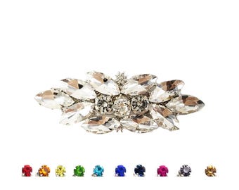 Op de afbeelding: Een zilverkleurige strass-versiering met een cluster van heldere kristallen in een bladvormig ontwerp. De versiering is perfect om kleding, accessoires of knutselwerk te versieren.